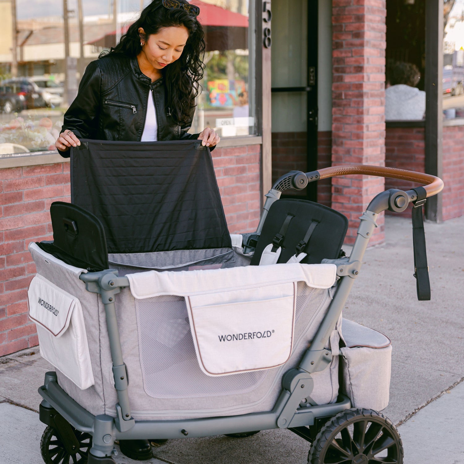 A woman setting up the WonderFold L2 stroller wagon by unfolding a wind and privacy shade.