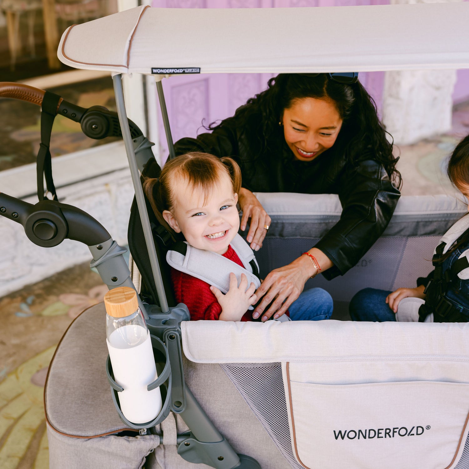 A toddler smiling while being securely strapped into the WonderFold L2 stroller wagon with the 5-Point Harness for safety