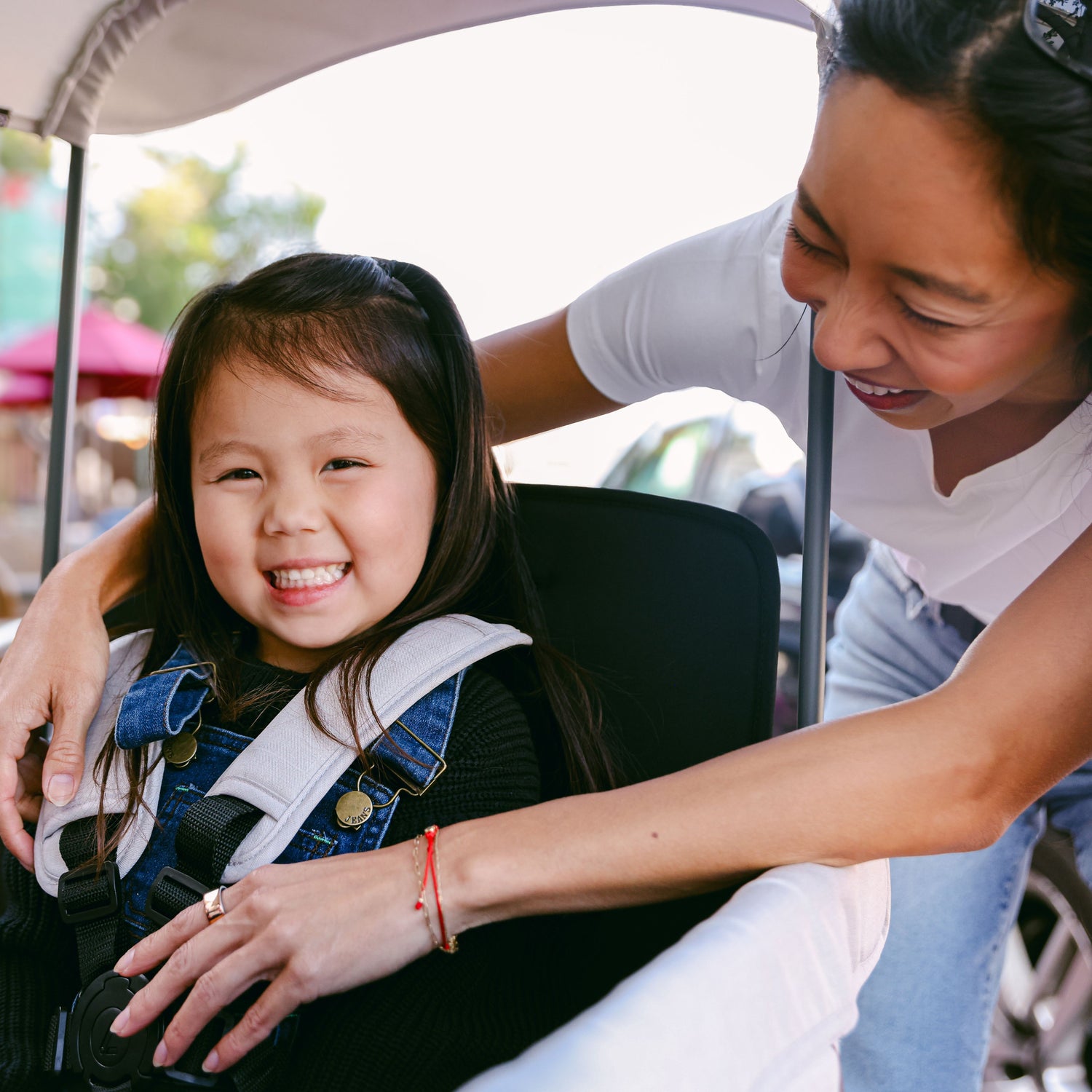 A little girl smiling while an adult securely fastens the 5-point harness on the WonderFold L2 stroller wagon.