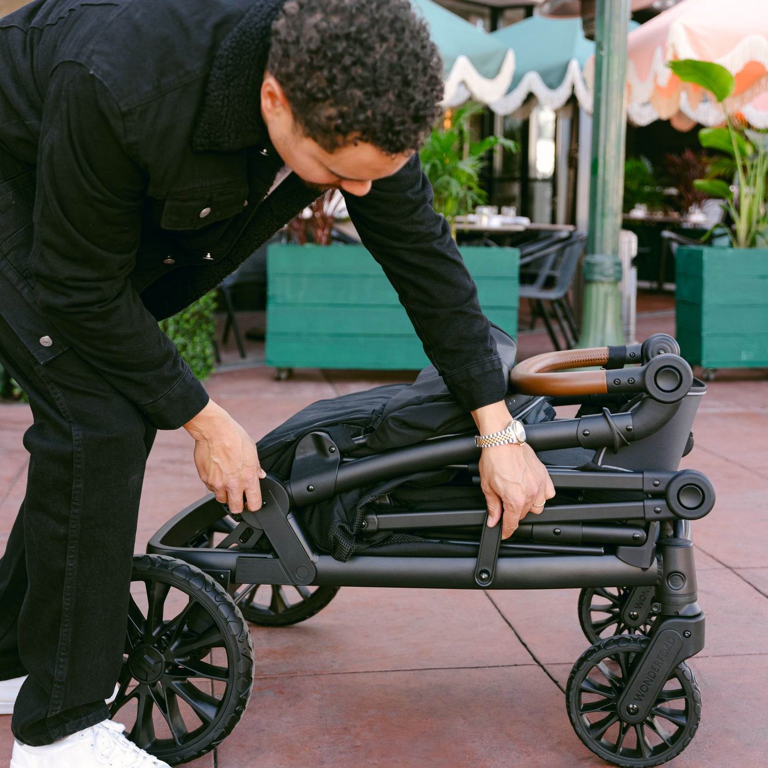 A man folding the WonderFold L4 stroller wagon, showcasing its compact and travel-friendly design.