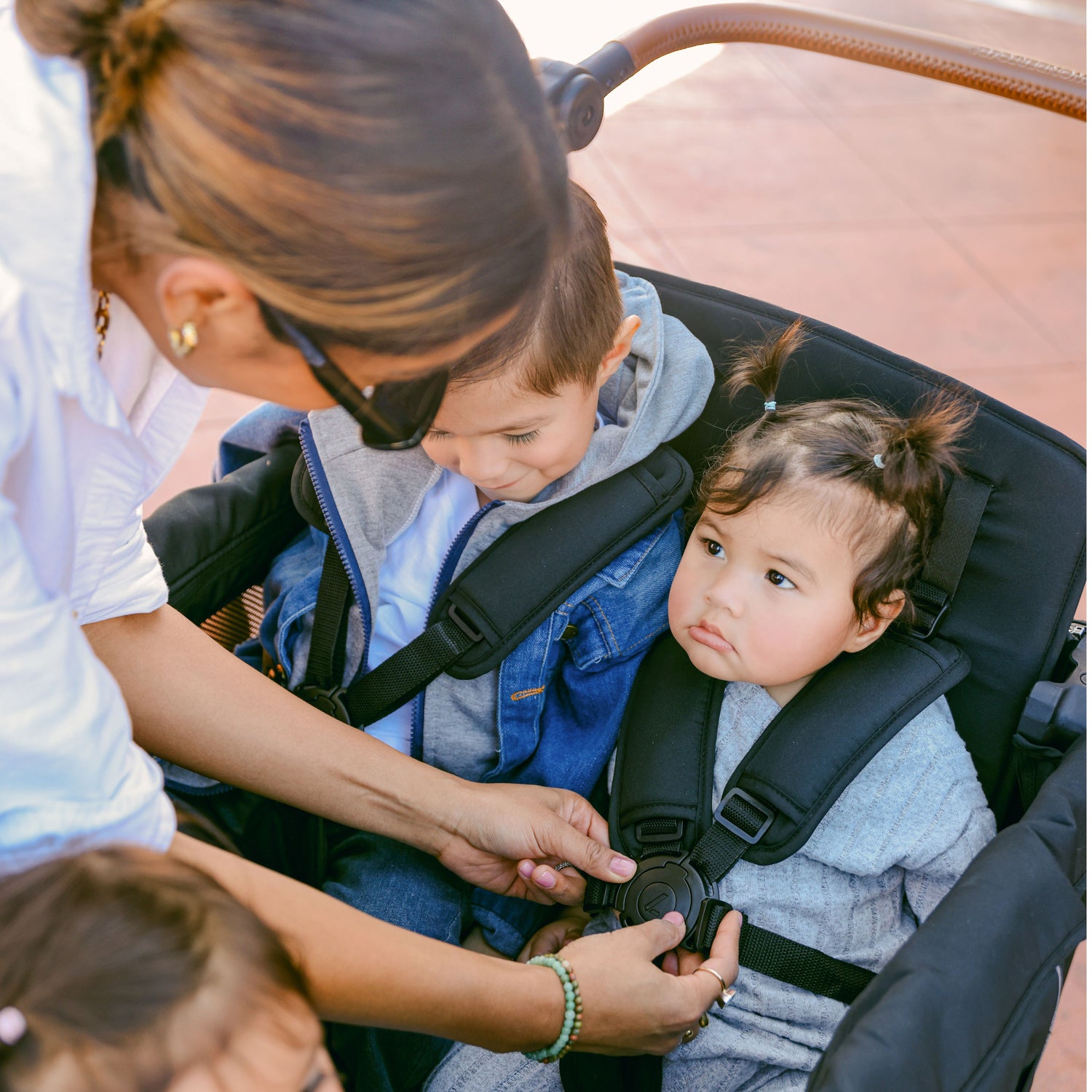 A mother securing two children in the WonderFold L4 stroller wagon with five-point safety harnesses.