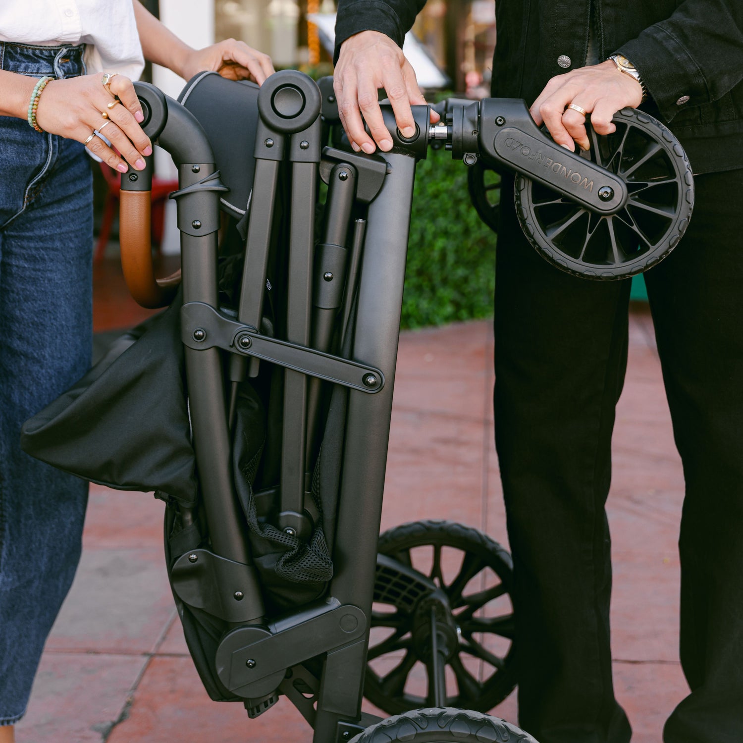 A couple folding the WonderFold L4 stroller wagon, showcasing its compact and travel-friendly design.