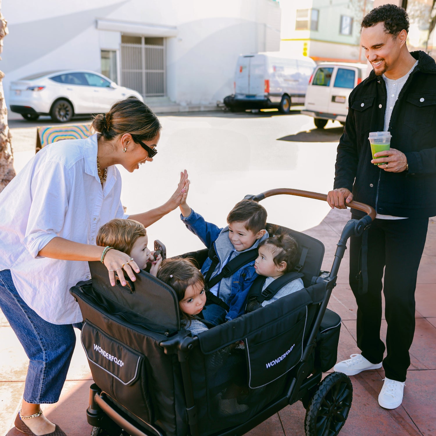 A mother high-fiving her child while they sit in the WonderFold L4 stroller wagon, with a father smiling in the background.