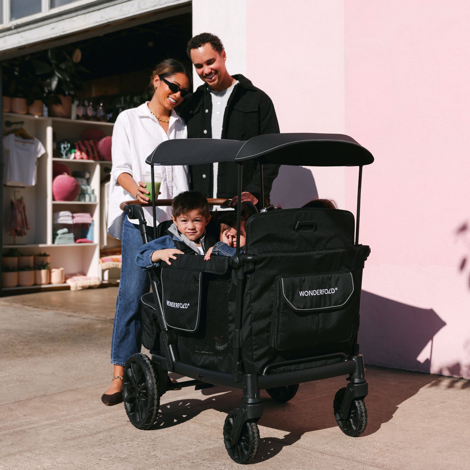 A family enjoying a stroll with the WonderFold L4 stroller wagon, featuring a black canopy and spacious seating.