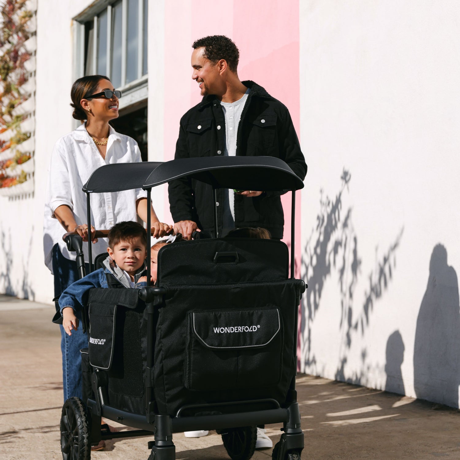 A family walking with the WonderFold L4 stroller wagon, highlighting its durable and stylish black design