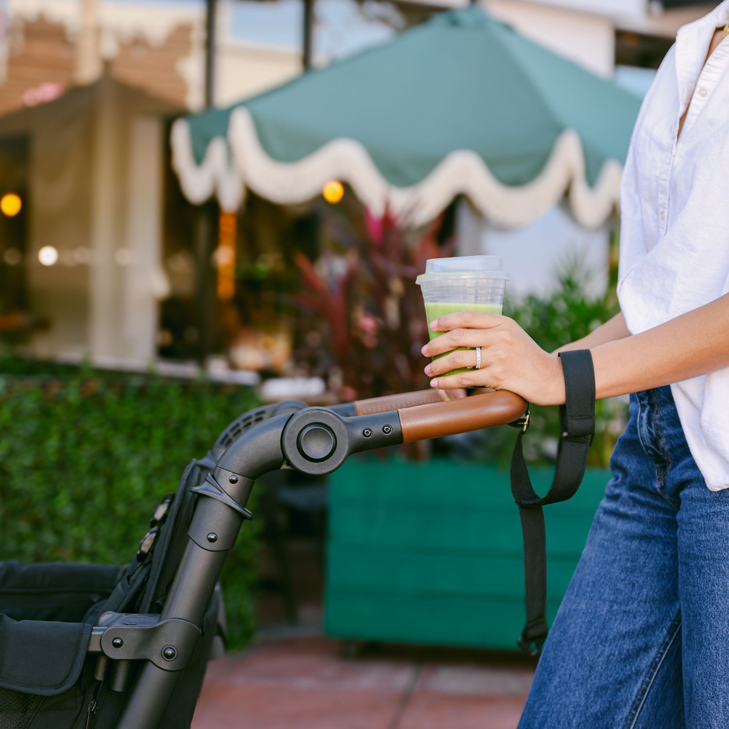 Close-up of a person holding a drink while gripping the faux leather handlebar of the WonderFold L4 stroller wagon with the safety strap.