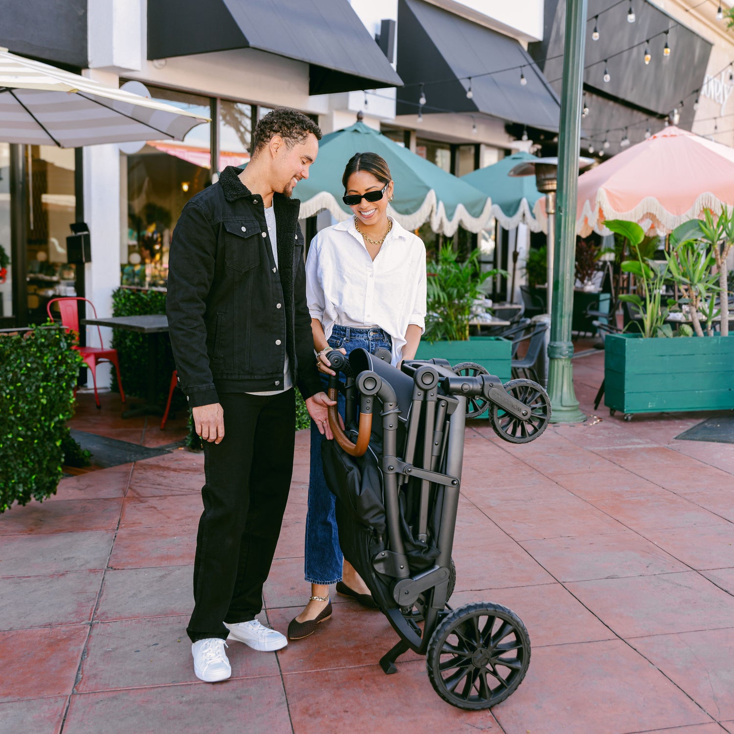 A couple standing next to the fully folded WonderFold L4 stroller wagon, showing its compact size.