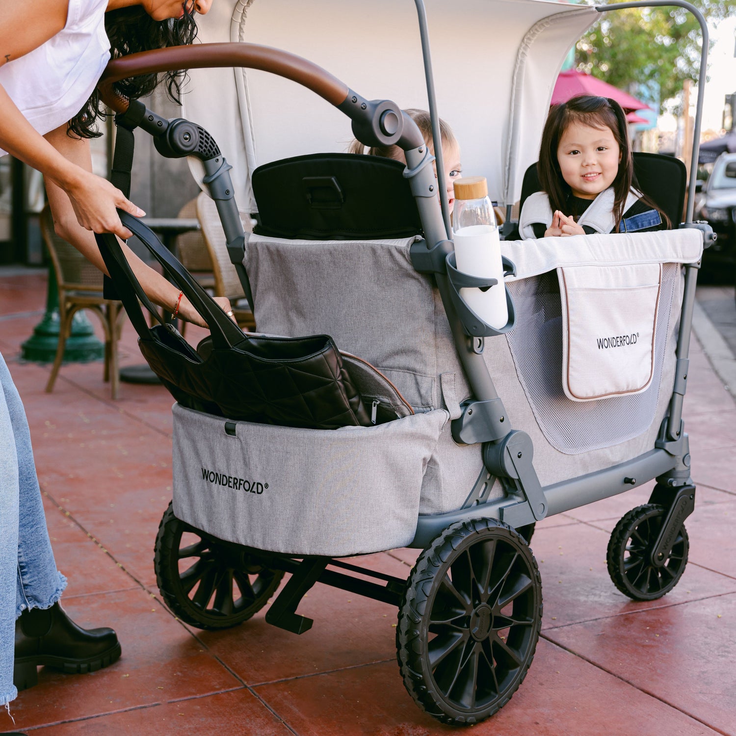 A woman placing her purse inside the rear basket of the WonderFold L2 stroller wagon while two children sit inside.