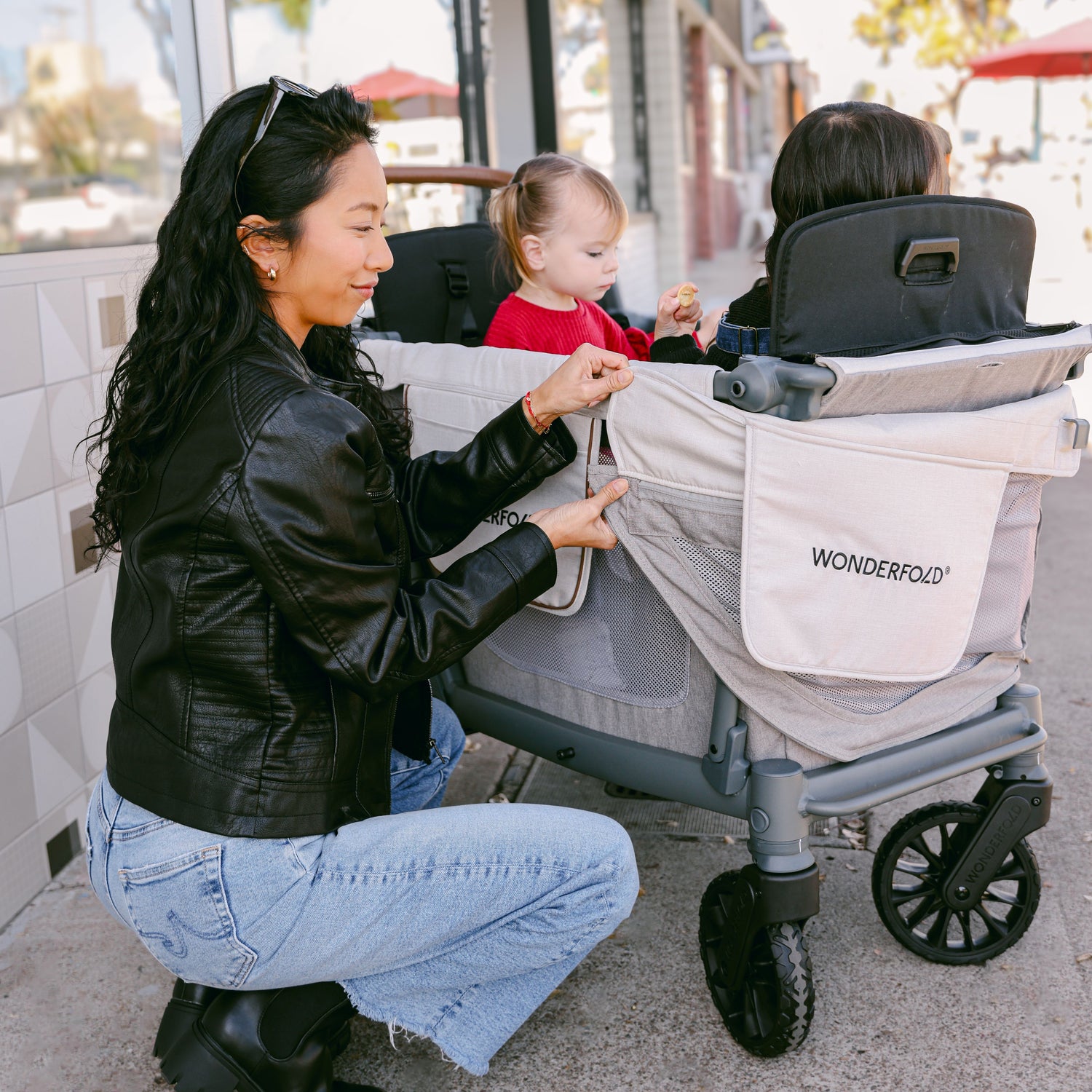 A woman adjusting the side mesh panel of the WonderFold L2 stroller wagon while two children sit comfortably inside.