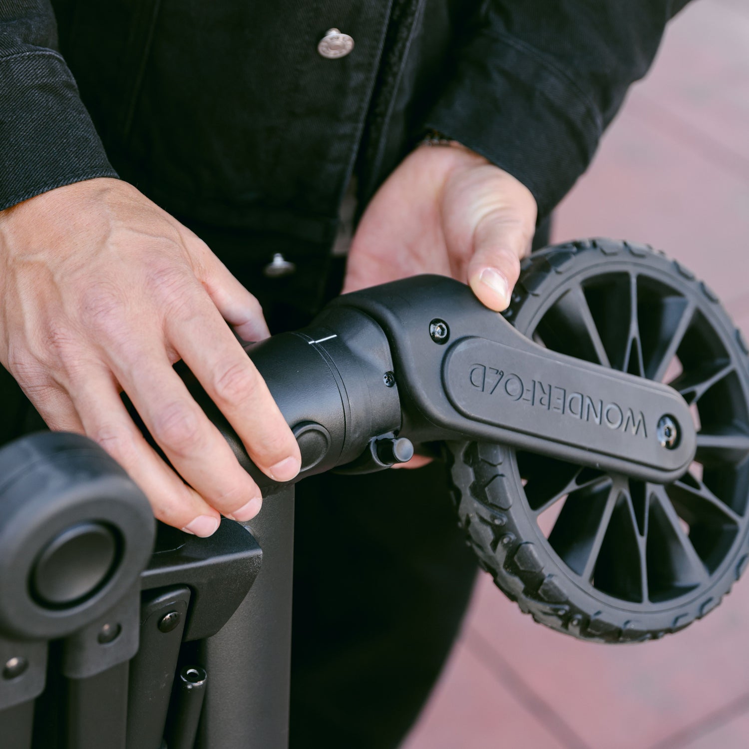 A man attaching the front wheel to the WonderFold L4 stroller wagon, using the quick release button.