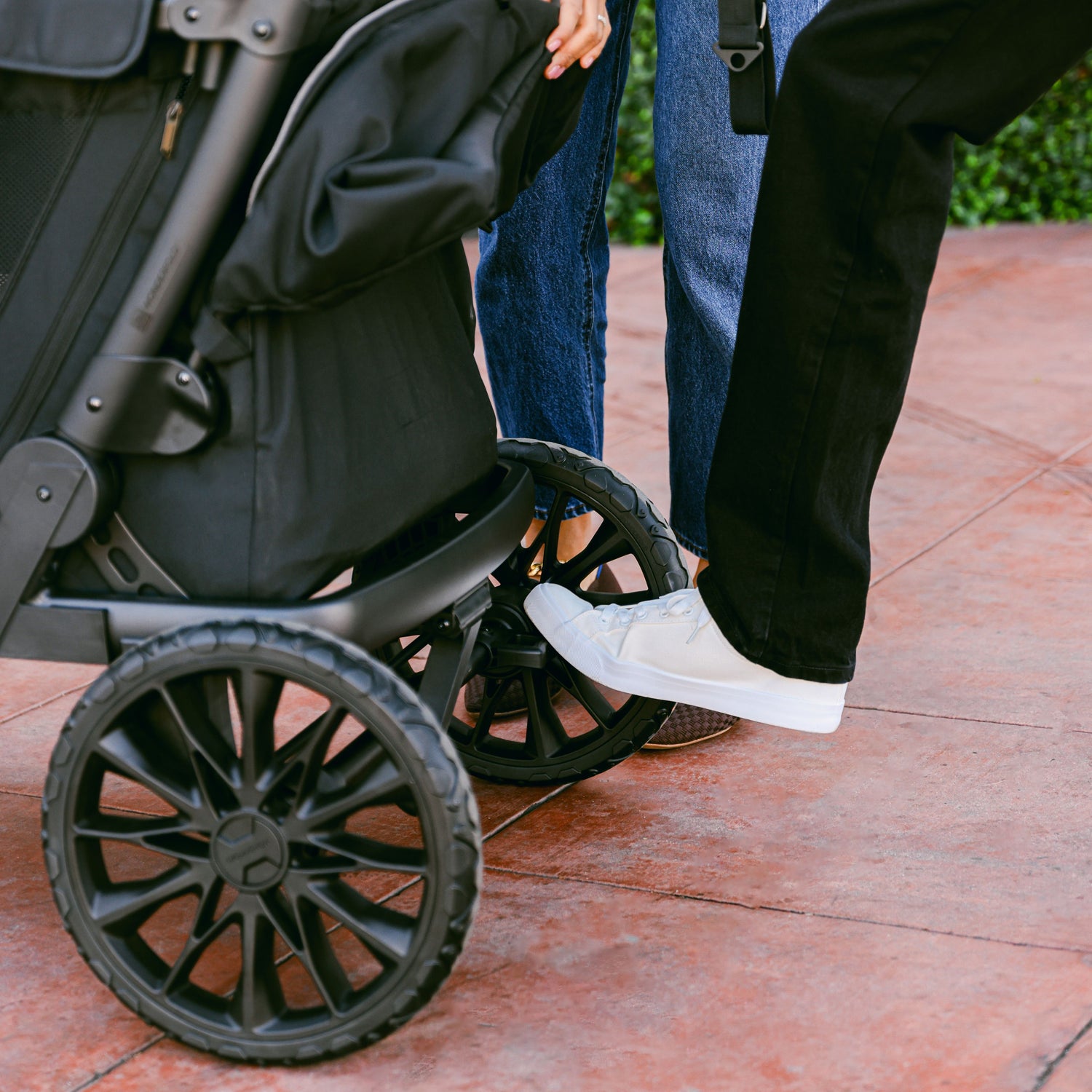 A person using their foot to engage the rear brake of the WonderFold L4 stroller wagon for added safety.