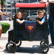 Family with children in a Superman-themed stroller on a city street.
