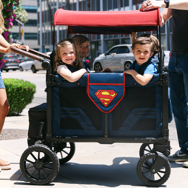 Family with children in a Superman-themed stroller on a city street.