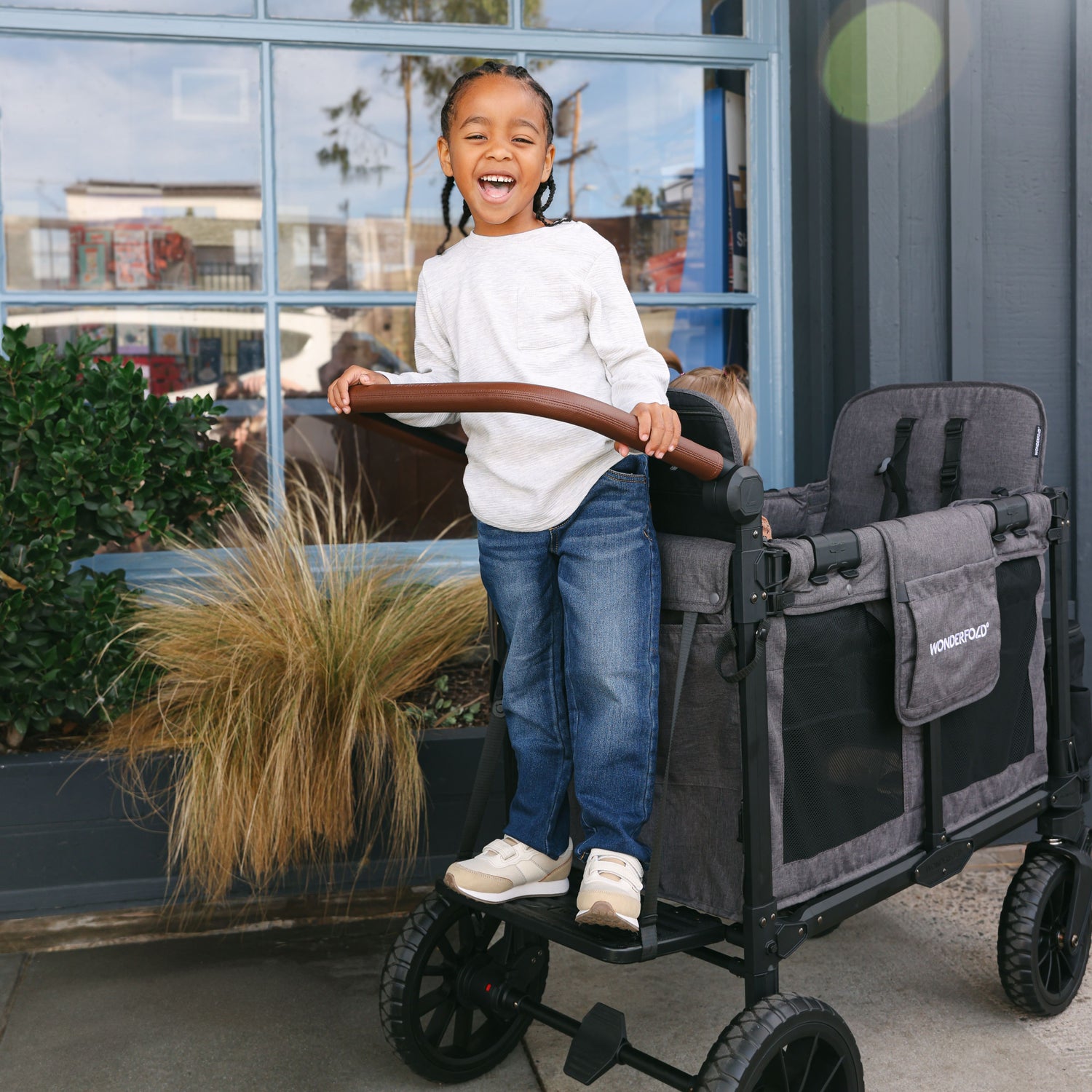 Child standing on the Buddy Board accessory, securely attached to a WonderFold W2 stroller wagon