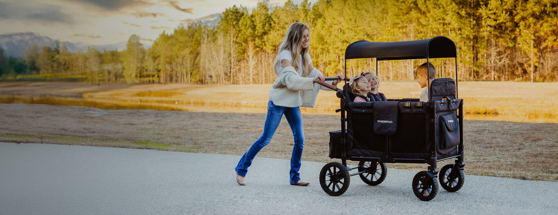 A parent walking outdoors while pushing children in a WonderFold stroller wagon