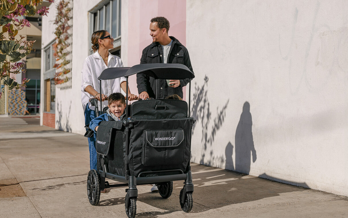 Parents walking a sidewalk with two kids riding in a WonderFold L Series wagon