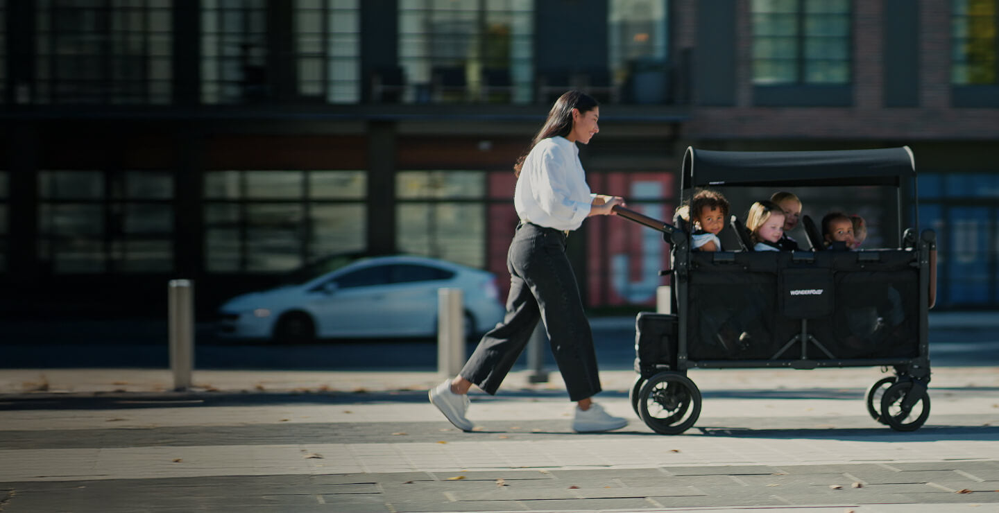 A parent walking outdoors while pushing children in a WonderFold stroller wagon
